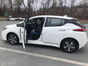 A person sits in the driver's seat of a white electric vehicle with the door open